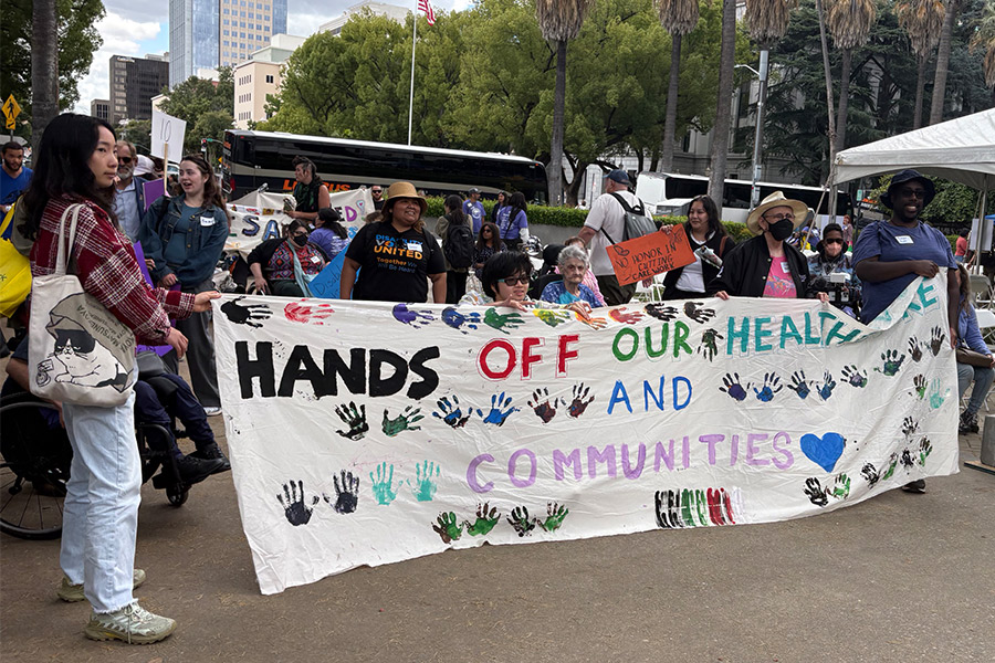 Protestors at CDLA Day of Action holding a fabric poster that says Hands Off Our Healthcare and Communities