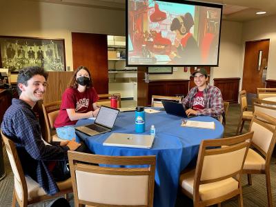 Three writing tutors sit around a table at a study jam event with lo-fi beats image on screen in background