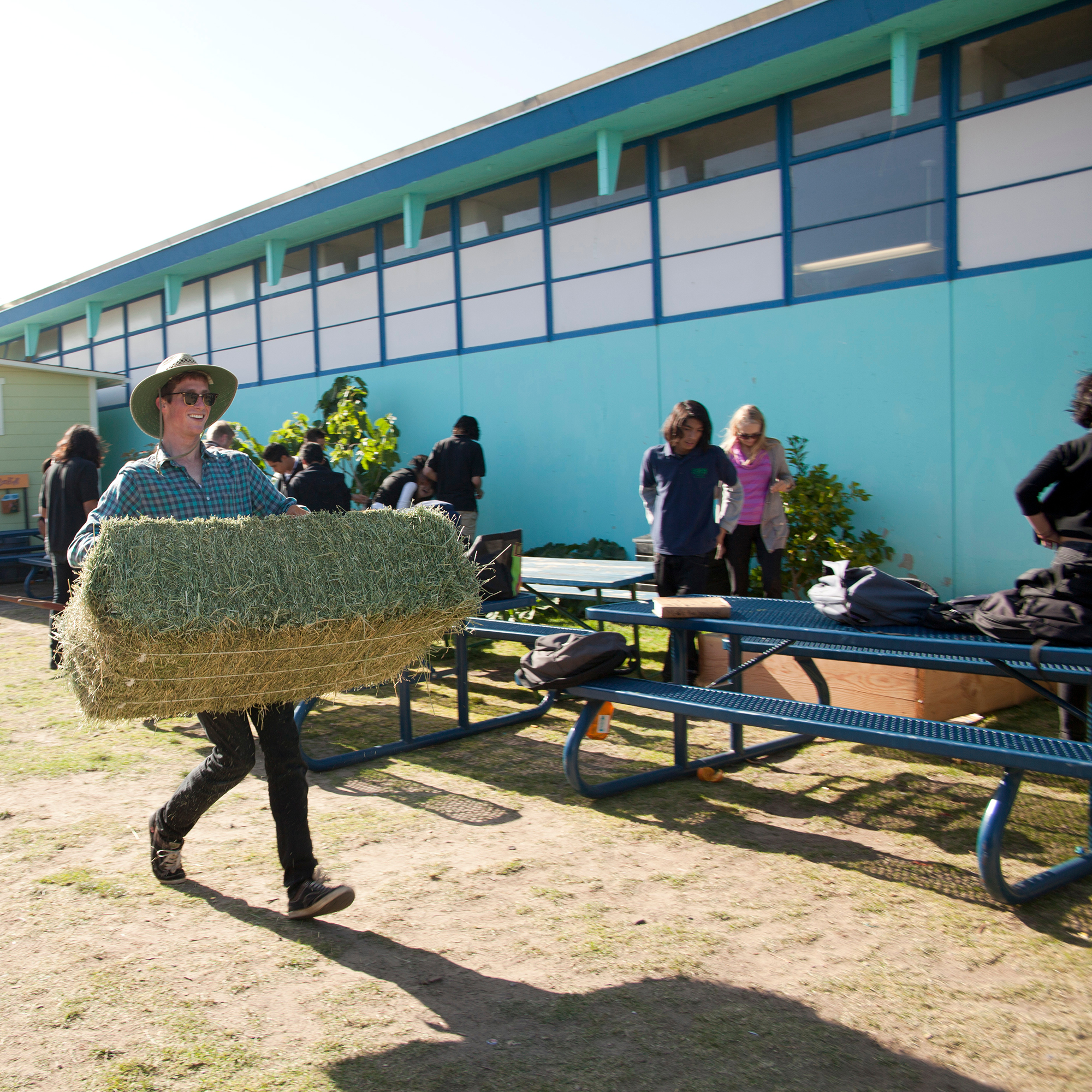student carrying haystack outside a farm, in the background are other students