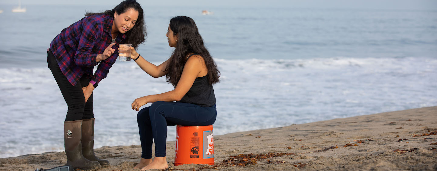 Female professor conducting research on the beach with a student
