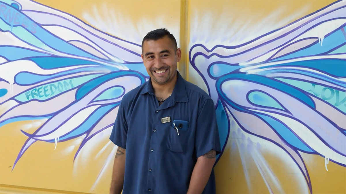 A person laughing while standing in front of a mural of angel wings
